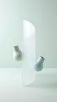 Minimalist still life composition featuring two sage green ceramic vases positioned against a white cylindrical column on neutral background, suitable for modern interior design and home decor projects.
