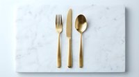 Gold flatware set with fork, knife, and spoon arranged on white marble surface for fine dining, table setting, and upscale restaurant design projects.
