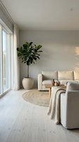Modern minimalist living room with beige sofa, fiddle leaf fig plant in ceramic pot, jute rug and natural light from large windows creating serene atmosphere.