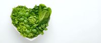 Fresh green lettuce and leafy vegetables arranged in heart shape on white background for healthy eating and nutrition concepts.