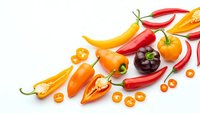 Colorful hot chili peppers variety including red, orange and yellow peppers scattered on white background for cooking and spice ingredient concepts.