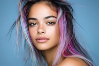 Young mixed race woman with vibrant pink and blue hair highlights against blue background, natural makeup, and confident expression showcasing modern beauty trends.