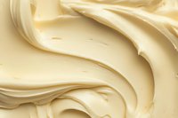 Creamy vanilla frosting swirls in smooth waves creating soft textured background pattern. Close up macro food photography shows rich buttery dessert topping detail.