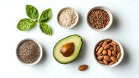 Fresh avocado half with raw almonds, chia, flax and sesame seeds arranged on white background with green basil leaves, healthy fats and omega sources.