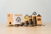 Wooden house models with stacked coins and calculator showing mortgage, real estate investment, property finance and home loan concepts.