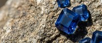 Blue sapphire gemstones on rough stone surface showcasing natural mineral formation and precious stone mining discovery for jewelry making applications.