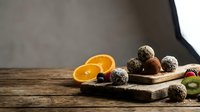 Homemade chocolate energy balls with coconut coating on wooden cutting board next to fresh orange slices for healthy snacking and dessert preparation.