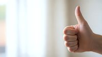 Hand showing thumbs up gesture against blurred background expressing approval, success and positive feedback for business and communication concepts.