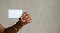 Hand holding blank white card against neutral beige background, suitable for business branding, marketing mockups, and promotional material presentations.