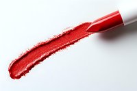 Red lipstick smear on white background with cosmetic pencil creating vibrant streak of color, close-up macro shot showing texture and pigment detail.