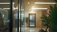 Modern office interior with glass walls and doors, green plants, and soft lighting creating professional atmosphere for business environment.