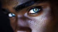 Close-up portrait of young African American man with striking blue eyes and water droplets on face showing intense emotional expression and natural skin texture.
