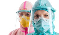 Medical workers wearing protective equipment including face shields, surgical masks, and protective gowns during pandemic response. Focus on female healthcare staff.