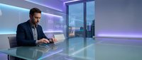 Professional businessman working on laptop in modern futuristic office with holographic displays and neon lighting for corporate technology presentations.