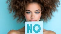 Young African American woman with natural curly afro hair and bright blue eyes holding NO sign against turquoise background, expressing serious confident look.