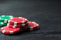 Stack of red and green poker chips on dark wooden surface with dramatic lighting and shallow depth of field, capturing casino gaming atmosphere.