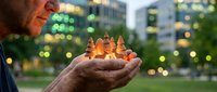 Middle-aged Caucasian man holding miniature wooden Christmas trees in cupped hands outdoors at dusk with bokeh city lights background for holiday concepts.