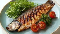 Grilled whole sea bass with crispy charred skin served on blue plate with fresh arugula salad and cherry tomatoes, restaurant quality seafood dish.