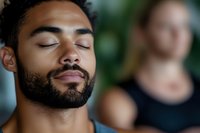 Young African American man with closed eyes and beard practicing mindfulness meditation in peaceful indoor setting with blurred background.