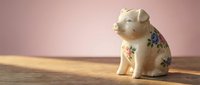 Vintage ceramic piggy bank with floral pattern sitting on wooden surface against soft pink background for savings and financial planning concepts.