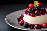 Elegant panna cotta dessert topped with fresh mixed berries including blackberries and cranberries on decorative plate for gourmet dining and culinary presentation.