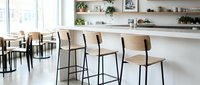 Modern bar stools with wooden seats and black metal frames arranged in bright kitchen space with white shelving and plants.