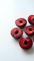 Fresh red plums cut in half showing juicy flesh and pits on clean white background for healthy eating and cooking concepts.
