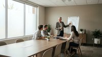 Mature male professional presenting business strategy to diverse team in modern office meeting room with whiteboard and natural light.