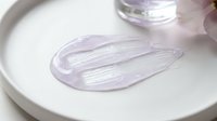 Transparent gel serum sample smeared on white plate, showing viscous cosmetic product texture for skincare formulation testing and beauty research applications.