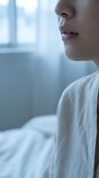 Close-up profile of young woman's lips and nose in soft morning light by window wearing white clothing for skincare and beauty concepts.