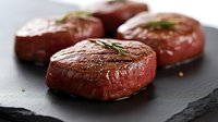 Rare medium beef steaks with rosemary garnish on dark slate plate, ready for fine dining presentation or restaurant menu use.