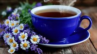 Steaming hot tea in cobalt blue cup with fresh daisies and lavender flowers on rustic wooden table, cozy morning atmosphere with natural light and steam.