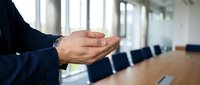 Professional businessman with clasped hands in modern conference room ready for corporate meeting or business presentation in office environment.