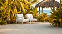 Tropical beach resort lounge chairs under palm trees with thatched umbrella overlooking turquoise ocean waters for luxury vacation relaxation.