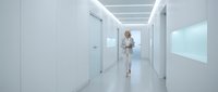Woman in white lab coat walking through modern sterile corridor with glass doors and bright LED ceiling lights, suitable for healthcare, medical facility, and corporate office design projects.
