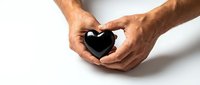 Male hands gently holding black heart shape against white background symbolizing love, care, protection and emotional support for healthcare concepts.