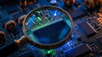 Magnifying glass focusing on microchip circuitry with glowing green and blue circuit pathways, representing technology inspection, quality control, and digital innovation for tech industry applications.