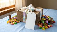 Kraft paper gift box with pastel ribbon and blank tag surrounded by colorful candy on blue tablecloth near sunny window for celebrations and holidays.