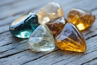 Colorful polished gemstones and crystals on rustic wooden surface with natural lighting, showcasing translucent minerals in amber, blue, and clear tones.
