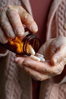 Senior woman pouring white capsules from amber prescription bottle into palm, close-up view of aged hands in soft lighting, healthcare concept.