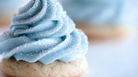 Blue frosted cupcake with sparkly swirl topping on blurred background for bakery dessert celebration party sweet treat baking concept.