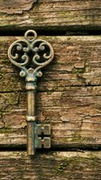 Ornate vintage brass key with decorative scrollwork lying on weathered wooden planks with peeling paint and moss growth for antique design projects.