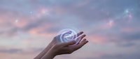 Hand holding glowing email symbol against dreamy twilight sky with soft clouds and sparkles for digital communication and marketing concepts.