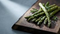 Fresh green asparagus spears with sea salt and herbs on rustic wooden cutting board, healthy organic vegetable ingredient for cooking and meal preparation.