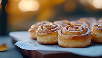 Fresh baked cinnamon rolls with sweet glaze icing on rustic wooden board, selective focus on golden pastry swirls against warm bokeh background.