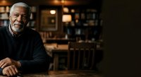 Senior African American man with gray hair smiling at wooden table in warm-lit home interior, suitable for lifestyle and family content.