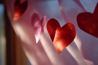 Red paper heart decorations casting soft shadows in warm sunlight, creating romantic Valentine's Day atmosphere for greeting cards and festive designs.