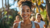 Young African American woman with curly hair in messy bun smiling brightly at camera during outdoor workout, wearing gray tank top, natural beauty and fitness lifestyle concept.