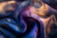 Luxurious silk fabric with iridescent purple and blue colors in macro shot showing detailed textile texture and flowing curves with golden light reflections.
