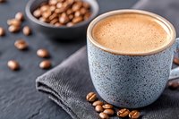 Fresh creamy coffee with frothy foam in blue ceramic cup on dark background with roasted coffee beans, morning beverage photography.